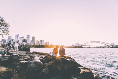 人们坐在岸边，站在悉尼歌剧院附近观看日落全景摄影